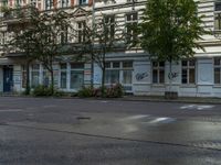 a stop light sits in front of two buildings in the city street, near a parked car and a few bushes