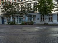 a stop light sits in front of two buildings in the city street, near a parked car and a few bushes