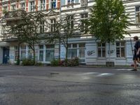 a stop light sits in front of two buildings in the city street, near a parked car and a few bushes