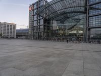 the outside of an architectural building with a few people inside it at dusk, on a plaza in front of a train station