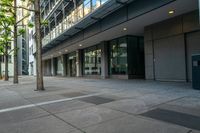 an empty street with tall buildings behind it and sidewalk area in front of the building