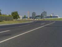 the street with two cars is empty in front of some city buildings by water in a sunny day