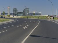 the street with two cars is empty in front of some city buildings by water in a sunny day