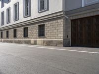 a white building on a street with wood garage doors in front of it and another building next to it