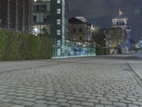 a sidewalk in a public area near a building and a tower at night with lights on