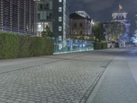 a sidewalk in a public area near a building and a tower at night with lights on