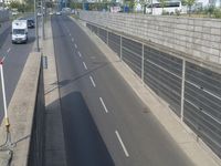 a street with a long fence with a car in it and other cars on the side of it