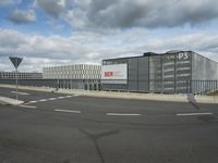 an empty street near a very large building under a blue sky with some fluffy clouds