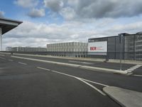 an empty street near a very large building under a blue sky with some fluffy clouds