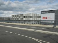 an empty street near a very large building under a blue sky with some fluffy clouds