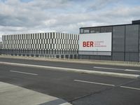 an empty street near a very large building under a blue sky with some fluffy clouds