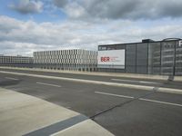 an empty street near a very large building under a blue sky with some fluffy clouds