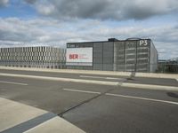 an empty street near a very large building under a blue sky with some fluffy clouds