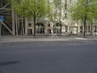 this picture shows two trees on the sidewalk in front of a building with green leaves