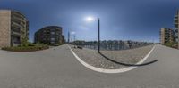 a fisheye lens photo of buildings on a brick road next to the water and sky