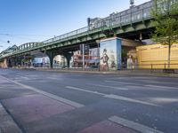 a view of an empty street, under an overhead bridge in a city, from the street with pedestrian and sidewalk markings