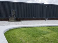 a tree with three small green trunks in front of an industrial building with black walls and grey stairs