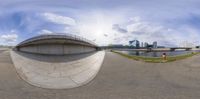 a street view looking up at a curved concrete ramp with a bridge across the water