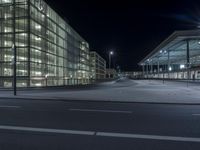 an empty empty parking lot with illuminated glass walls and street lamps nearby by night time