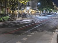 the road is covered in cars near parked bicycles and tall buildings at night time with many lights