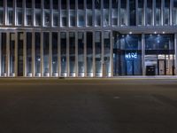 a car is parked in front of an office building at night time, with a bicycle chained to the post