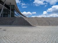 a person on a bike walking through a stone building entrance, in front of an enormous glass wall and stairs