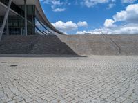 a person on a bike walking through a stone building entrance, in front of an enormous glass wall and stairs