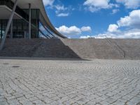 a person on a bike walking through a stone building entrance, in front of an enormous glass wall and stairs