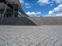 a person on a bike walking through a stone building entrance, in front of an enormous glass wall and stairs