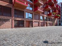 an empty brick sidewalk next to buildings and balconies in front of them with several chairs