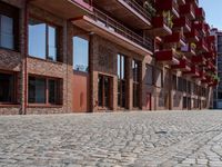 an empty brick sidewalk next to buildings and balconies in front of them with several chairs