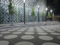 a sidewalk lined with trees next to an illuminated building with a large dot design in the center of the street