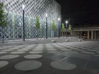 a sidewalk lined with trees next to an illuminated building with a large dot design in the center of the street