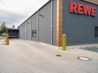 a red sign in front of a building that says rewe on it and a yellow and black pole by it