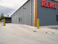 a red sign in front of a building that says rewe on it and a yellow and black pole by it