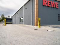 a red sign in front of a building that says rewe on it and a yellow and black pole by it