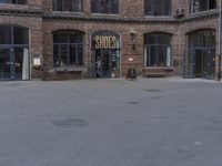 two people walking by the front of a brick building with an outdoor restaurant sign on the entrance