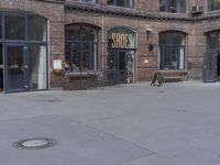 two people walking by the front of a brick building with an outdoor restaurant sign on the entrance