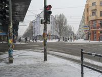 a traffic light on the corner of a snow covered street as people walk by at a busy intersection