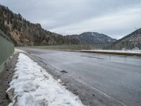 the asphalt is empty and the fence is completely empty of people and there are no people standing in the snow on the road