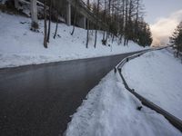 the road runs near some trees on a snowy hill side, with snow on the ground
