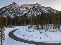 a car driving down the middle of a snow covered road with mountains in the background