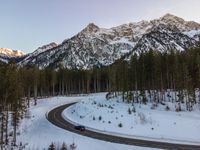 a car driving down the middle of a snow covered road with mountains in the background