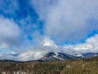 the view of some snow covered mountains and evergreen trees and a sky with clouds over the mountain range