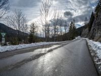 there is snow all over the asphalt of the mountain road in this picture you can see the road sign on the street below