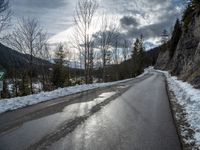 there is snow all over the asphalt of the mountain road in this picture you can see the road sign on the street below