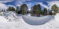 the skier is flying down the snow covered slope under a sky with clouds and trees