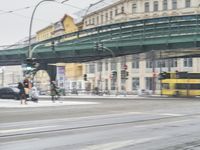 traffic lights, people and a car on a street with snow in front of an overpass