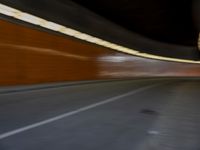 a man riding a skateboard down a city street next to a tall orange wall