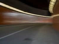 a man riding a skateboard down a city street next to a tall orange wall
